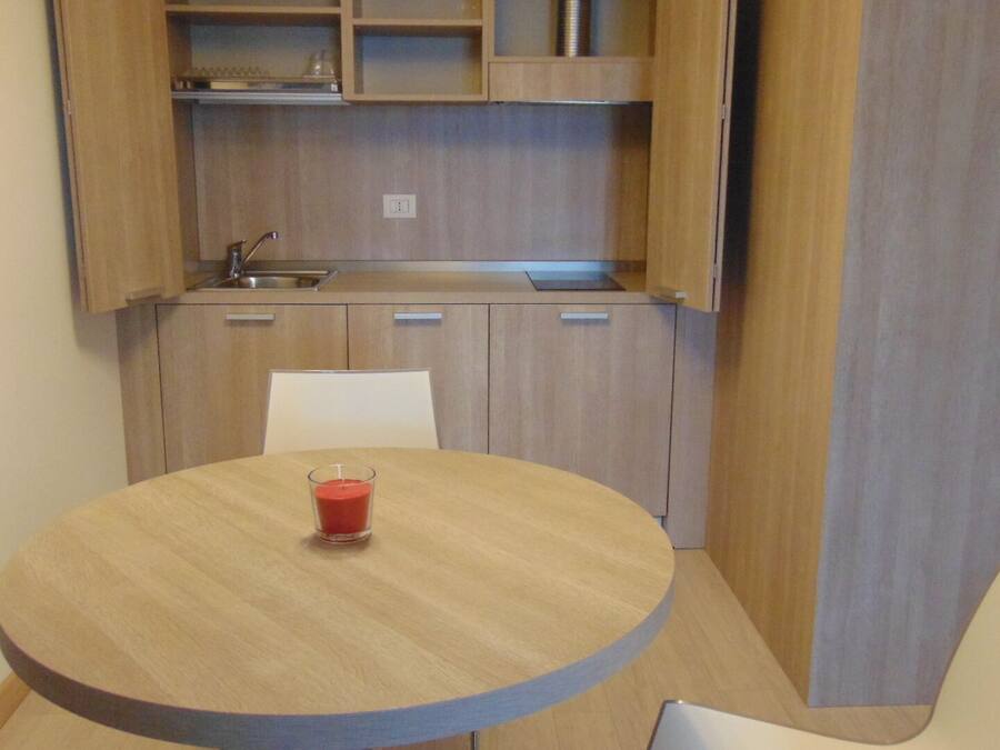 A compact kitchen with a sink, cabinets, and a round table with a glass of red drink.