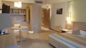 A hotel room with a bed, a small table with chairs, a kitchenette, and a bathroom.