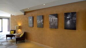 Un vestíbulo de hotel con piso a cuadros, una zona de estar con lámpara y cuatro fotografías blanco y negro en la pared.
