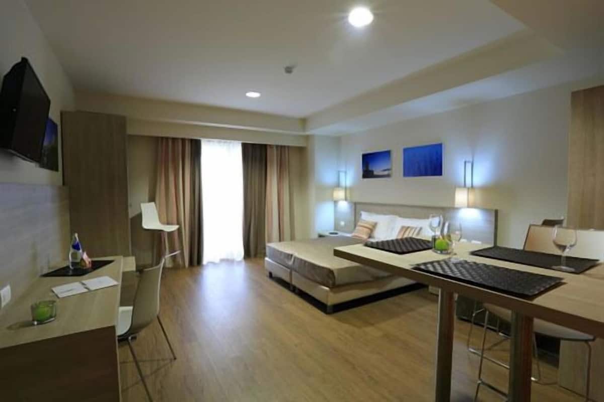 Habitación de hotel con escritorio, dos camas, televisor y ventana con cortinas.
