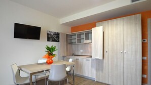 Una cocina moderna con horno empotrado, un comedor con mesa y sillas, y un televisor montado en la pared.