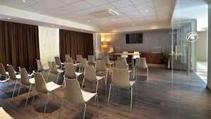 Un salón de conferencias con filas de sillas, un mostrador de recepción, un televisor de pantalla plana y un amplio ventanal con cortinas.