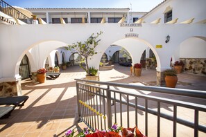 A courtyard with arches, potted plants, and a sign reading "APARTMENTOS LA BARANDA".
