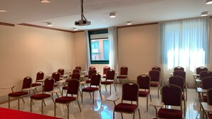 A conference room with rows of chairs and tables, a projector, and a large window with curtains. - Palace Hotel Legnano (Legnano)