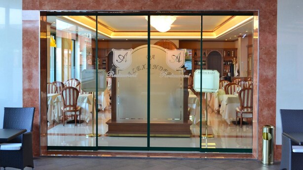 A restaurant with a glass entrance, wooden chairs, and a chandelier. - Palace Hotel Legnano (Legnano)