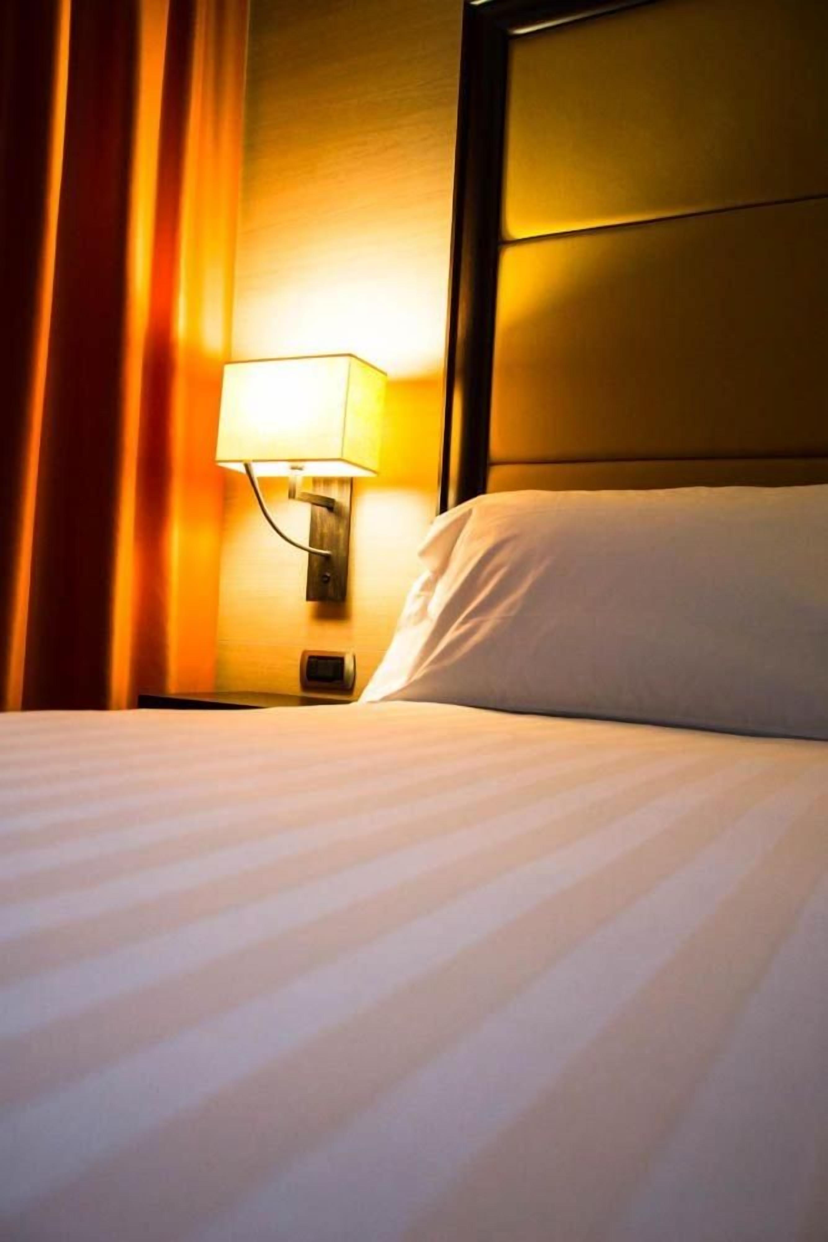 Una habitación de hotel con una cama, una mesita de noche, una lámpara y un cabecero.