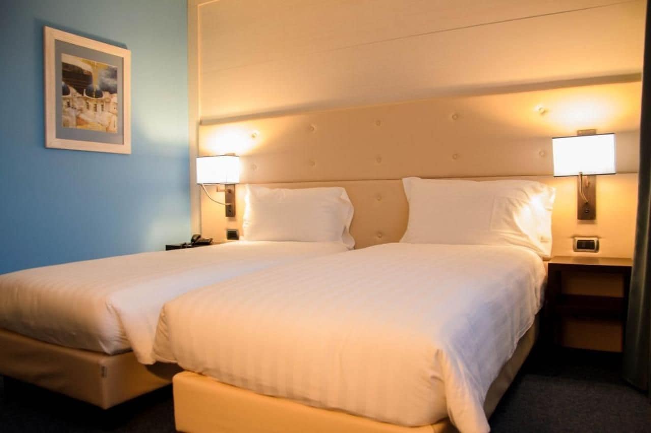 Una cama doble con cabecera, lámparas de noche y una mesita con un teléfono.