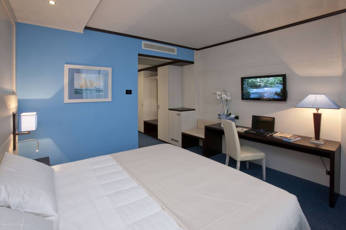 Ein Hotelzimmer mit einem Bett, einem Schreibtisch, einem Computer, einem Fernseher und einem Sessel.