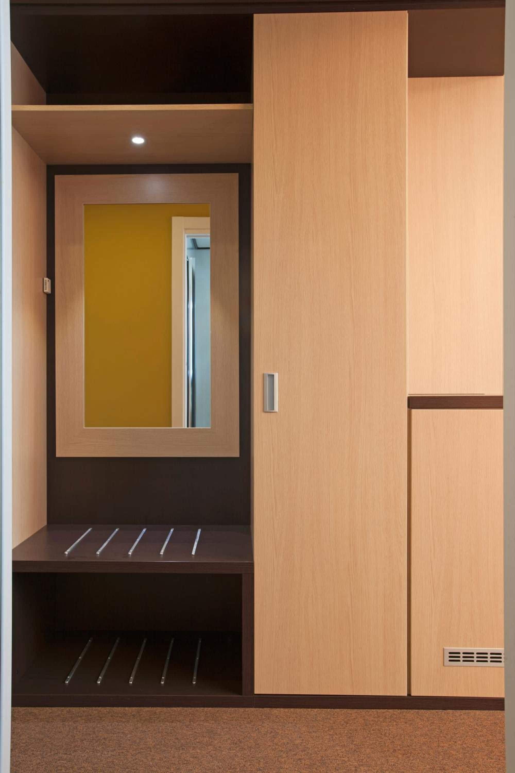 Un interior moderno con un armario de madera, un banco con barrotes metálicos y un espejo en la pared.