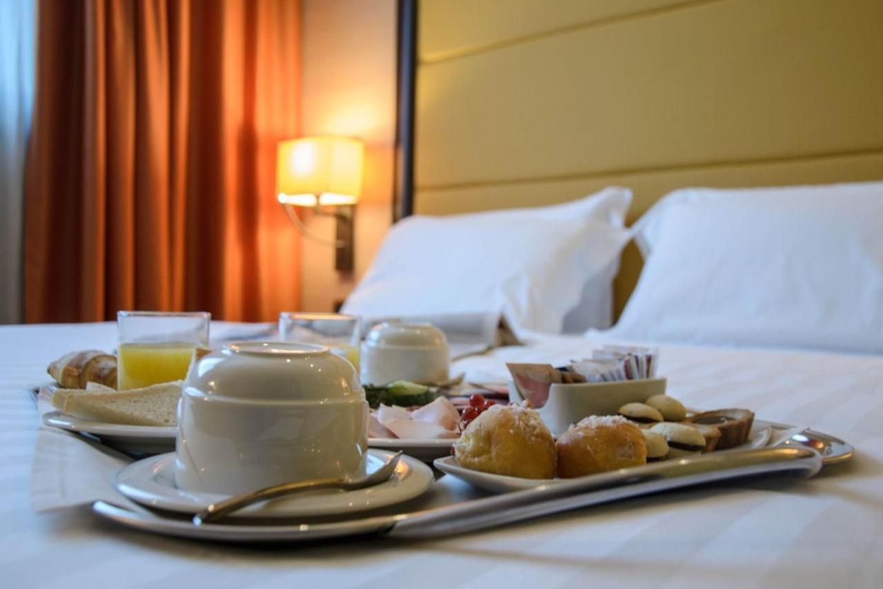 A neatly arranged breakfast tray on a hotel bed with a lamp in the background.