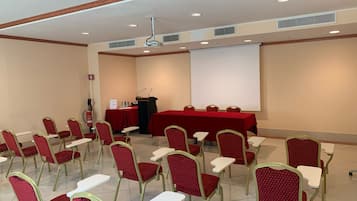 Un salón de conferencias con filas de sillas rojas, un atril y una pantalla grande.
