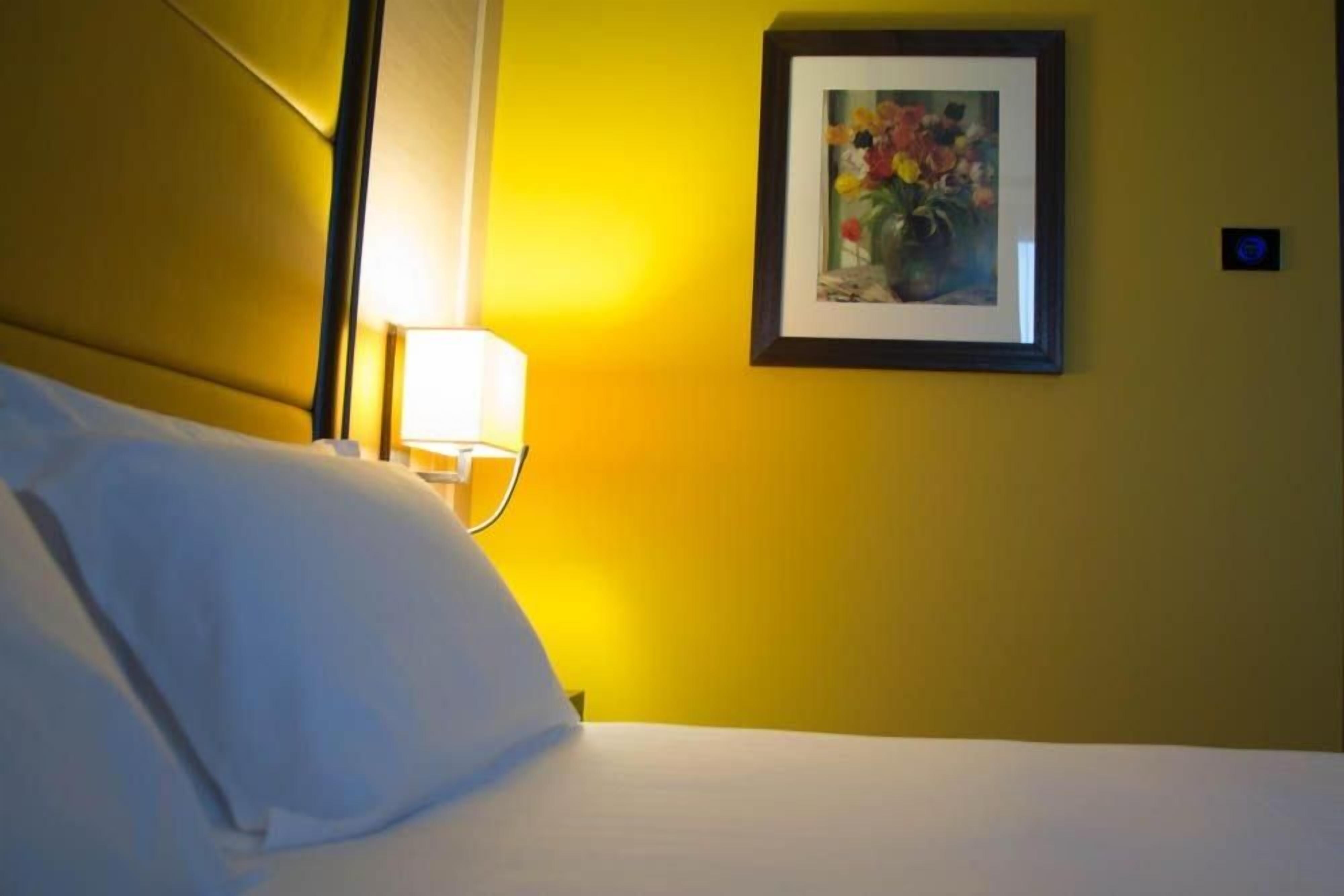 A hotel room with a bed, a nightstand with a lamp, and a framed picture on the wall.