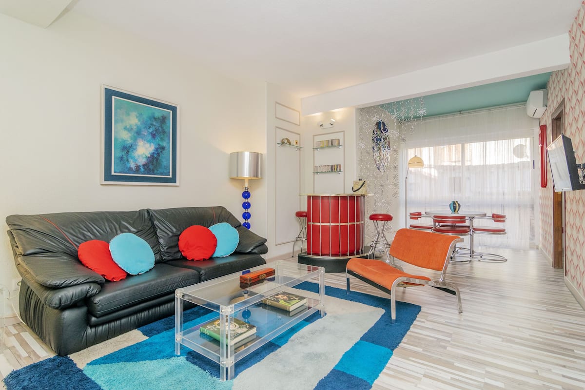 A modern living room with a black leather sofa, a glass coffee table, and a red drum set.