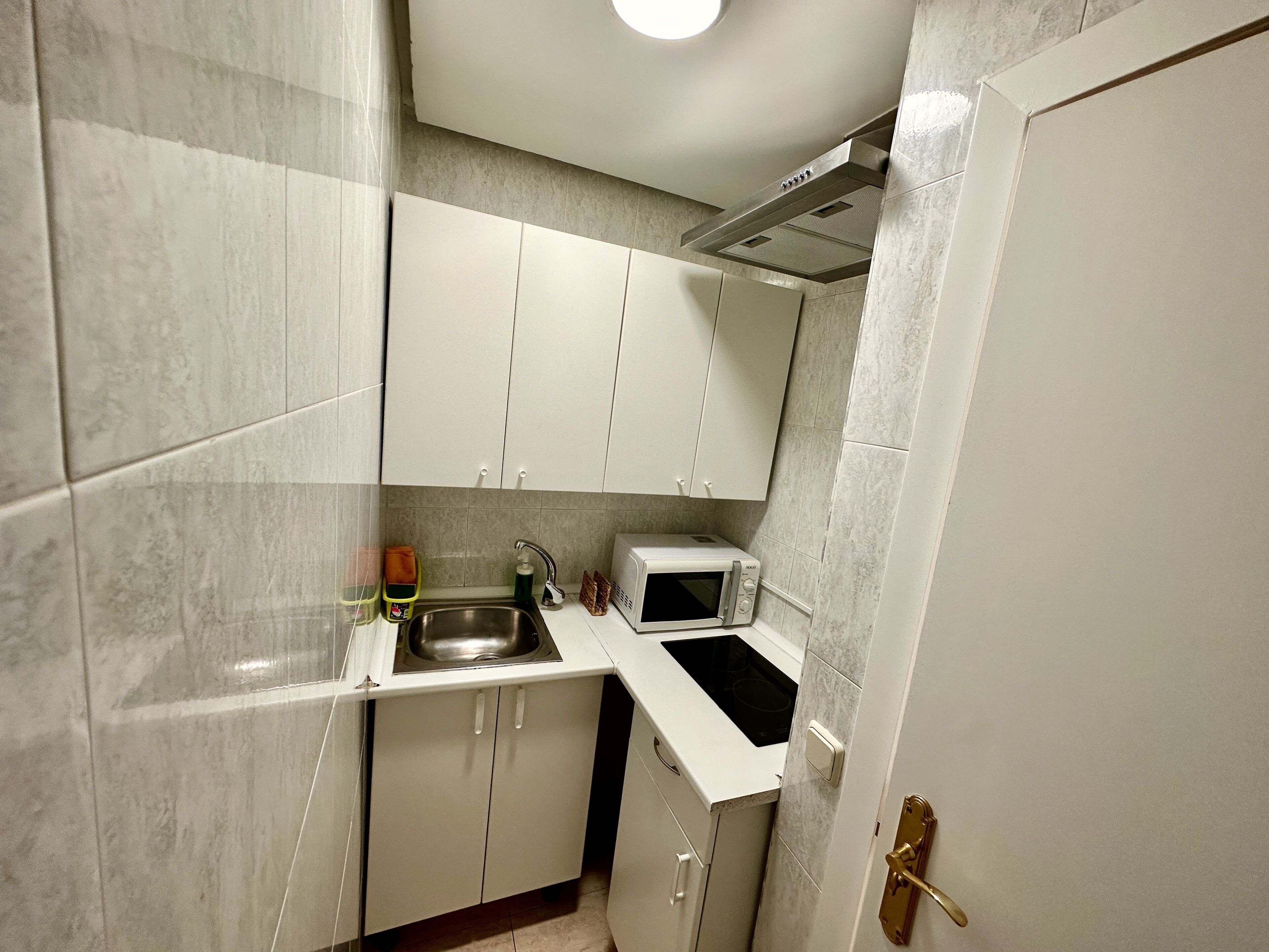 A compact kitchen with white cabinets, a stainless steel sink, a microwave, and a built-in stove.