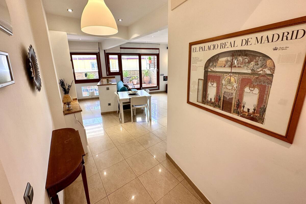 A modern interior with a dining area, a large framed picture of El Palacio Real de Madrid, and a pendant light.