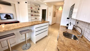 A modern kitchen with a granite countertop, white cabinetry, and a stainless steel sink. - Far Home Gran Vía - Hostel (Madrid)