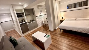 A compact hotel room with a kitchenette, a sofa, a bed, and a small table. - Far Home Gran Vía - Hostel (Madrid)