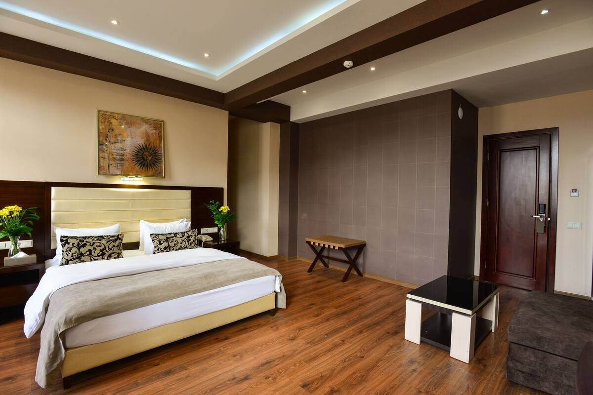 Una habitación de hotel moderna con una cama grande, mesitas de noche, una pequeña mesa y una puerta.