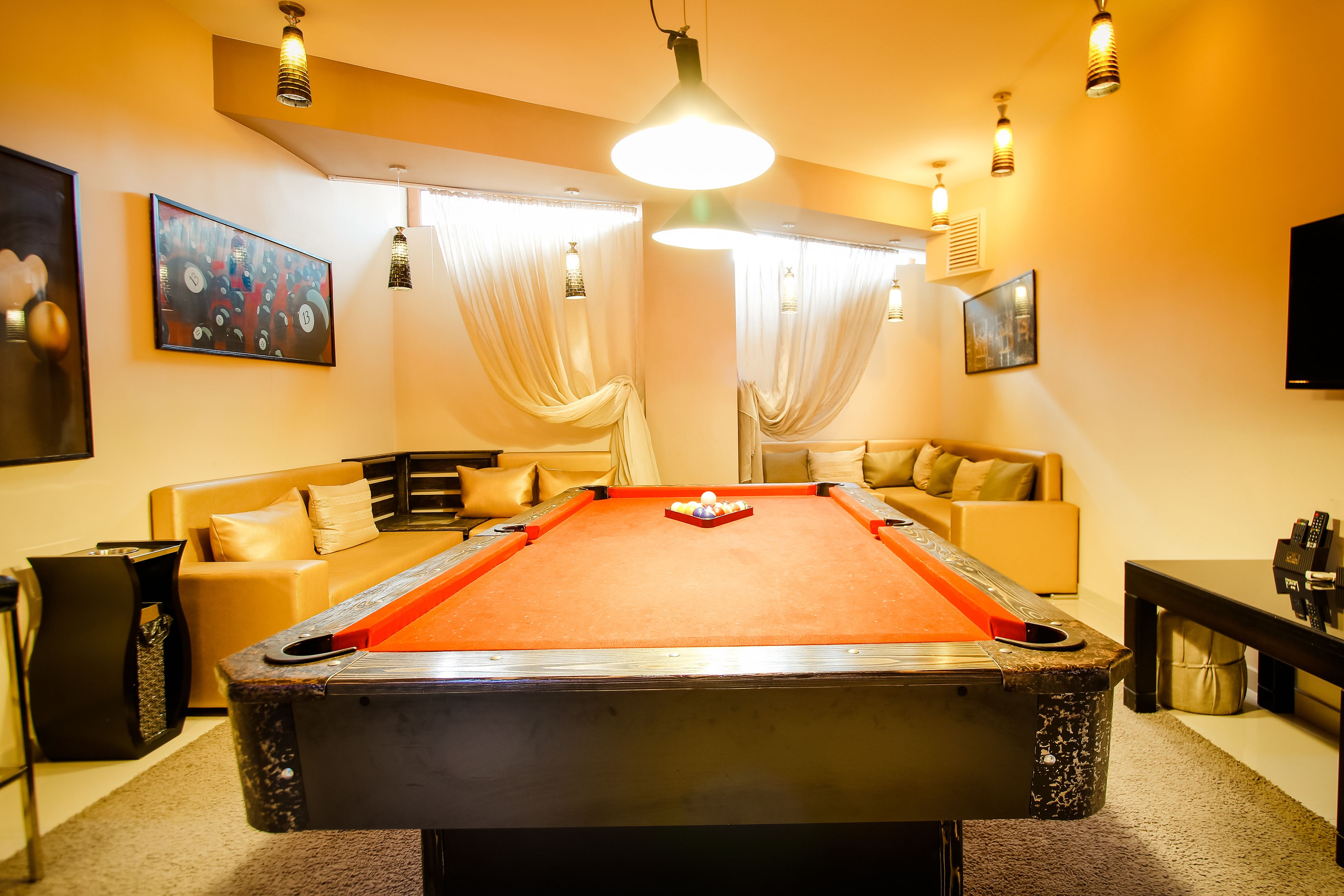 A pool table in a room with a sofa and cushions, a television, and artwork on the walls.