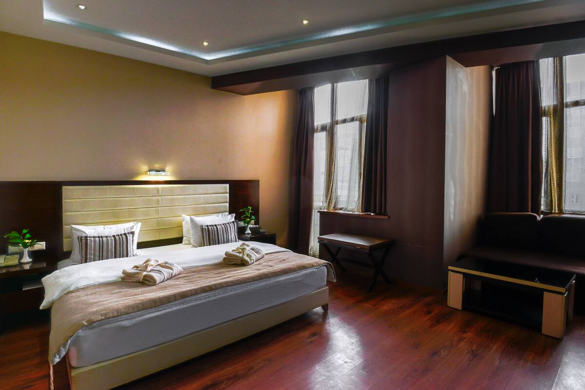 Habitación de hotel con una cama grande, un escritorio, una banca y una ventana con cortinas.