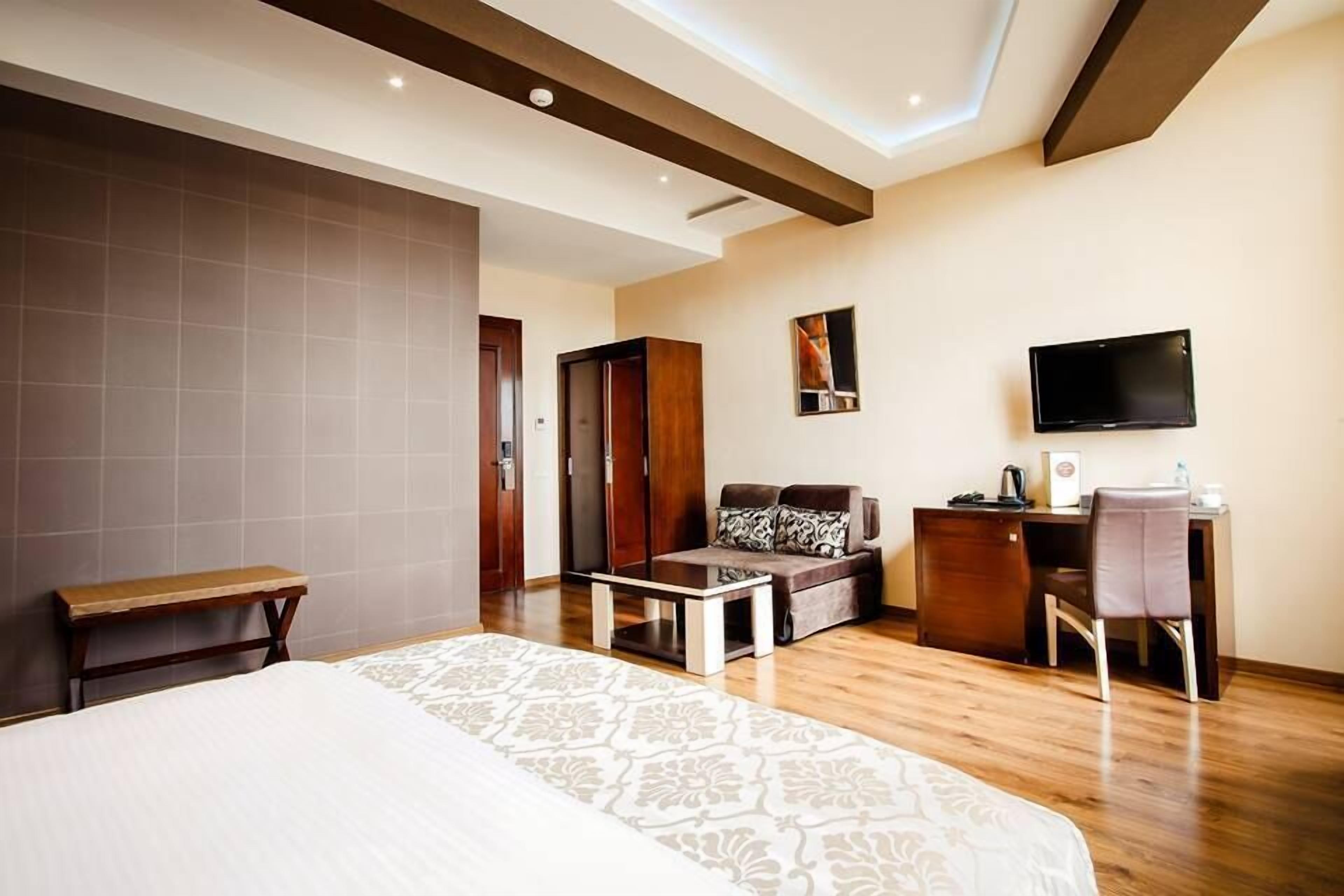 A hotel room with a bed, a desk, a chair, a sofa, and a TV.