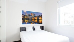 Una habitación de hotel con una cama grande, vista al cielo nocturno y un cuadro de paisaje urbano en la pared.