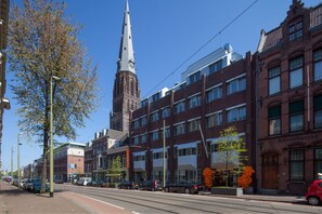 Une vue de rue avec un clocher d’église imposant, des bâtiments modernes et des voitures garées.