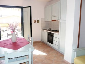 A compact kitchen with white cabinets, a stove, and a dining area with a table and chairs. - Sa Tanchitta (Valledoria)