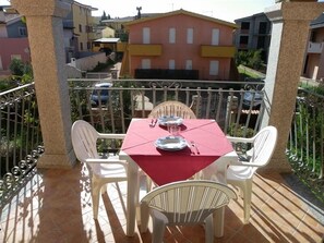A balcony with a table set for two, surrounded by white chairs, overlooking a residential area with colorful buildings. - Sa Tanchitta (Valledoria)