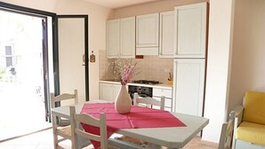 Uma sala de jantar com uma mesa posta para dois, um vaso com flores e um sofá amarelo.