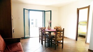 Uma sala de estar com sofá, uma mesa de jantar com cadeiras e uma porta de vidro deslizante que dá para uma varanda.