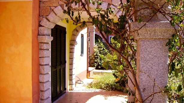 Uma entrada de pedra arqueada com porta e um pequeno jardim.