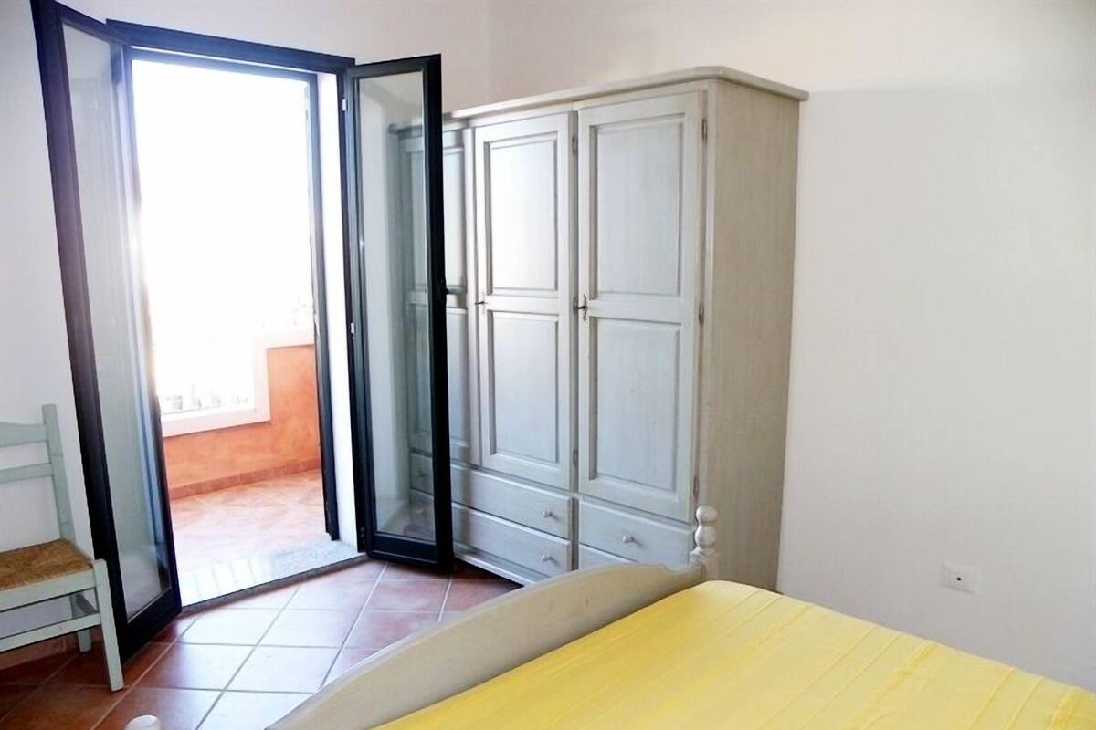 Un dormitorio con cama, armario y puerta corredera de vidrio que da a un balcón.