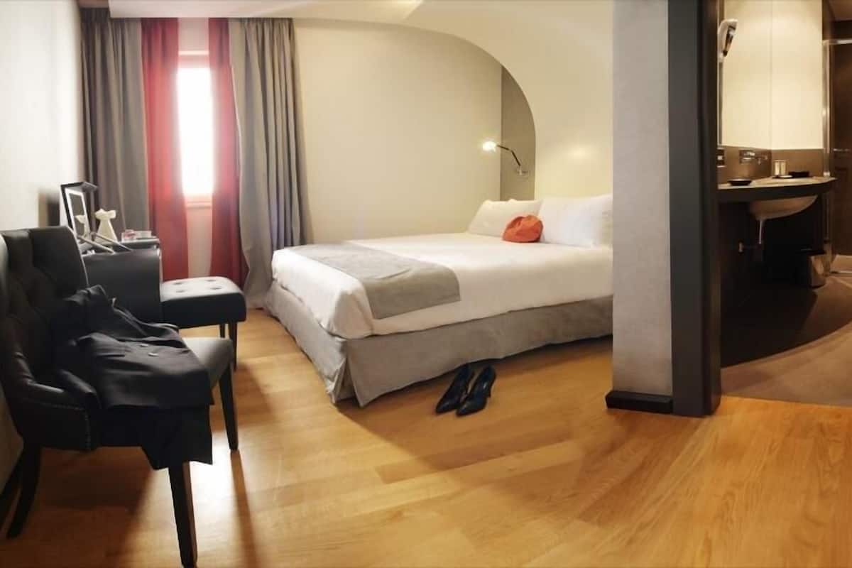 A hotel room with a bed, a desk, a chair, and a shower area.