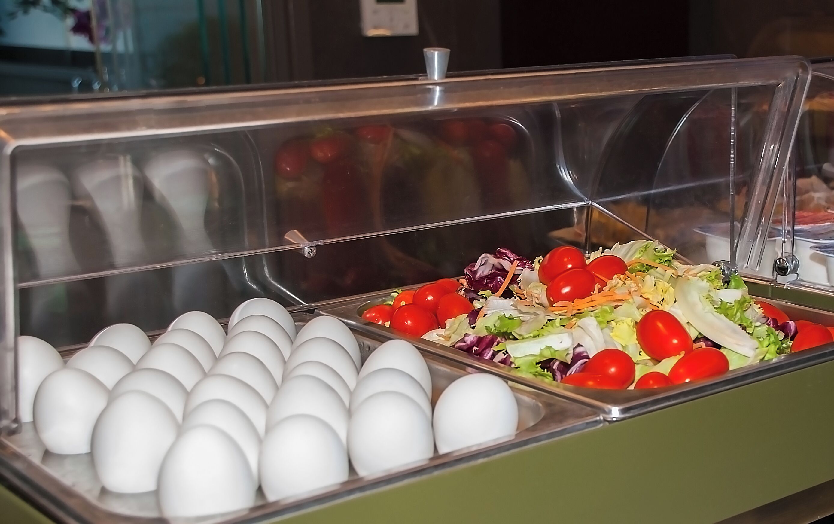 Buffet com diversos pratos, incluindo ovos e uma salada de tomate e alface.