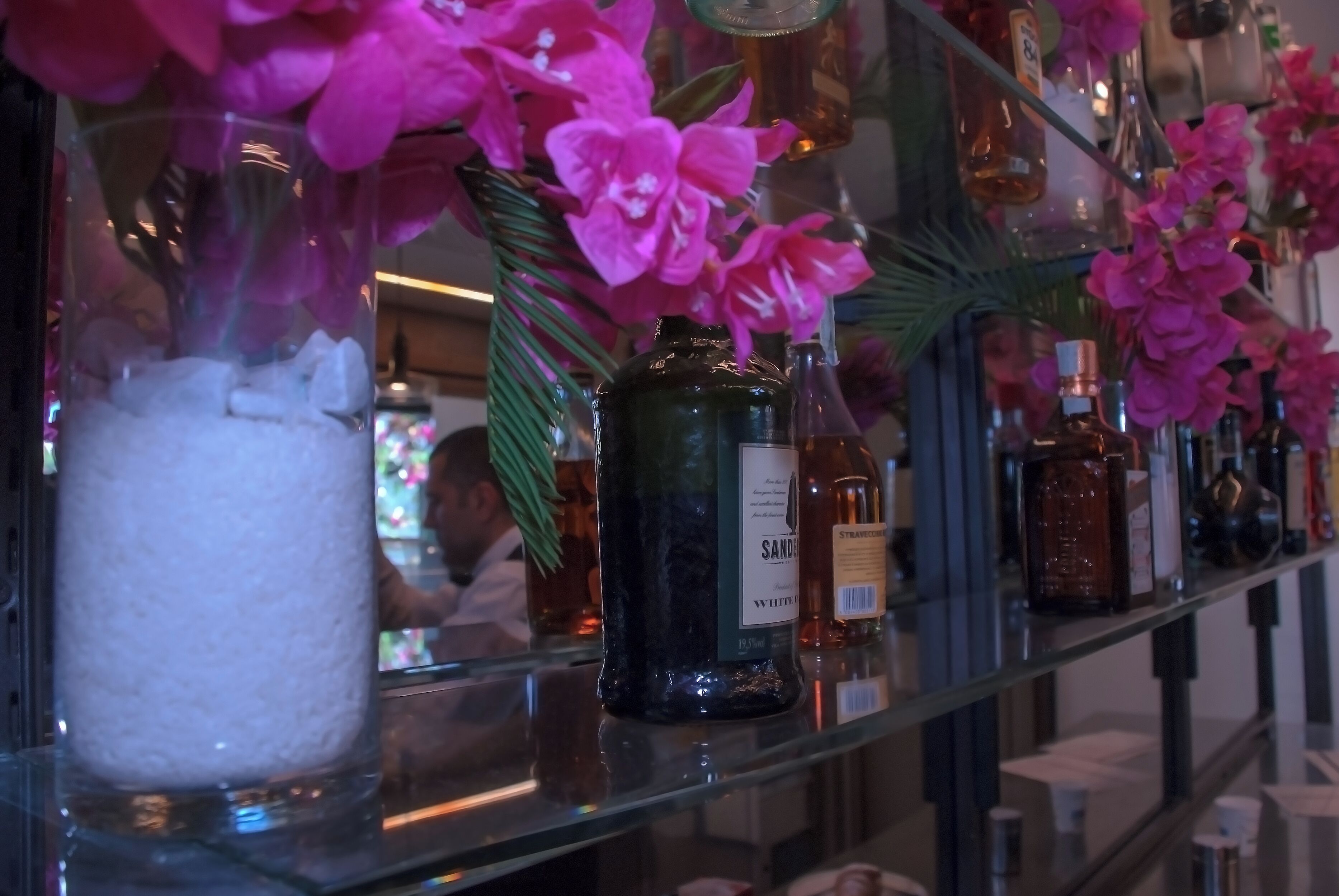 A bar area with shelves of liquor bottles and a glass vase with pink flowers.