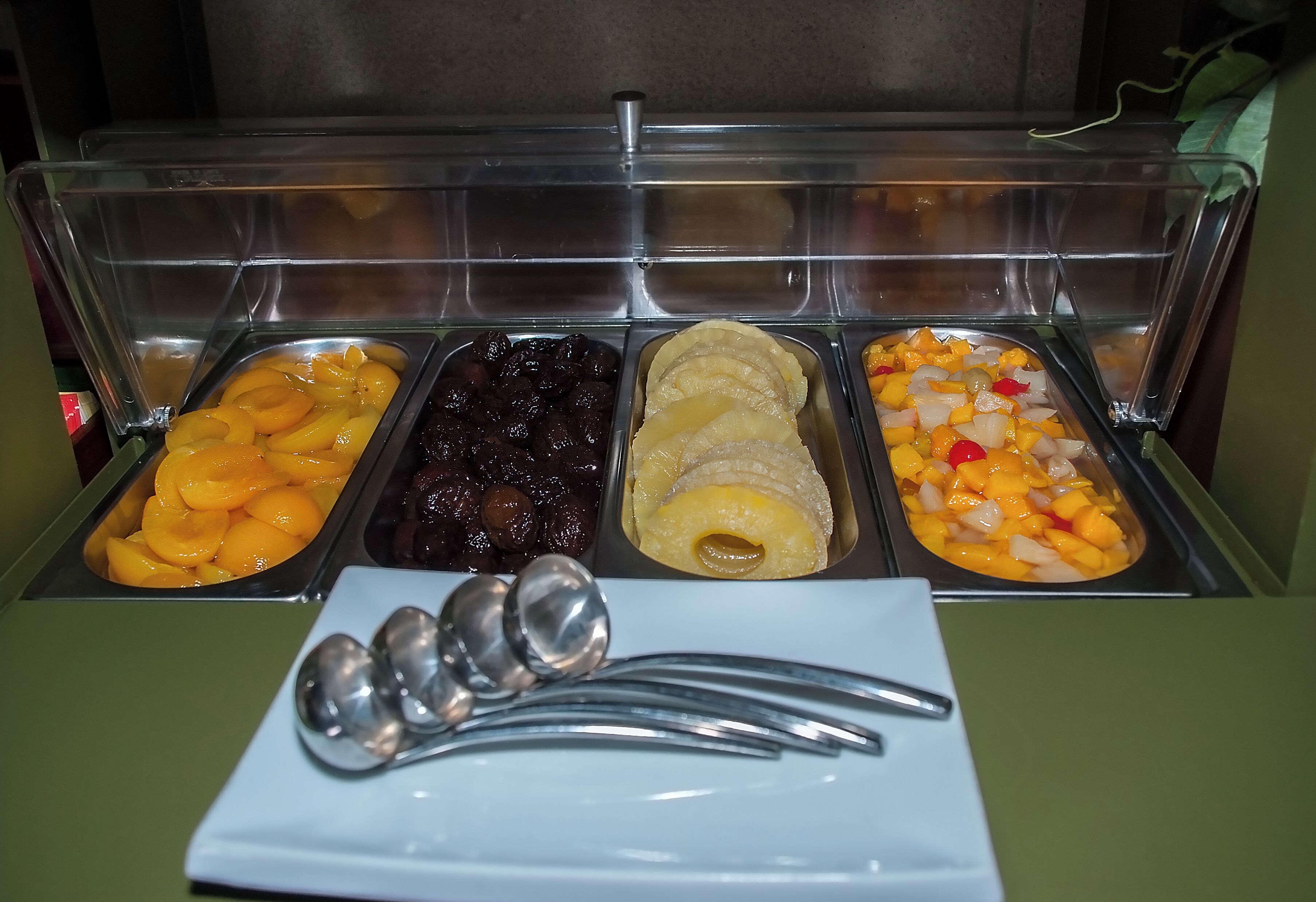A buffet with various fruit options and a plate with spoons.