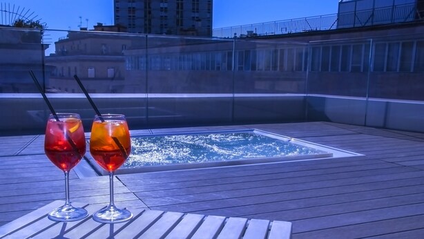 A rooftop terrace with two glasses of red beverages on a wooden table, overlooking a pool. - Culture Hotel Centro Storico (Naples)