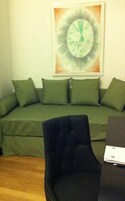 Una stanza con un divano verde, una poltrona nera e un quadro astratto incorniciato appeso al muro.