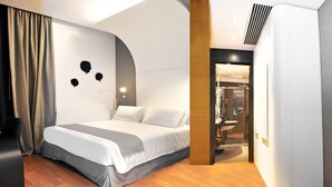 A modern hotel room with a bed, a curved wall design, a shower area, and a wooden floor. - Culture Hotel Centro Storico (Naples)