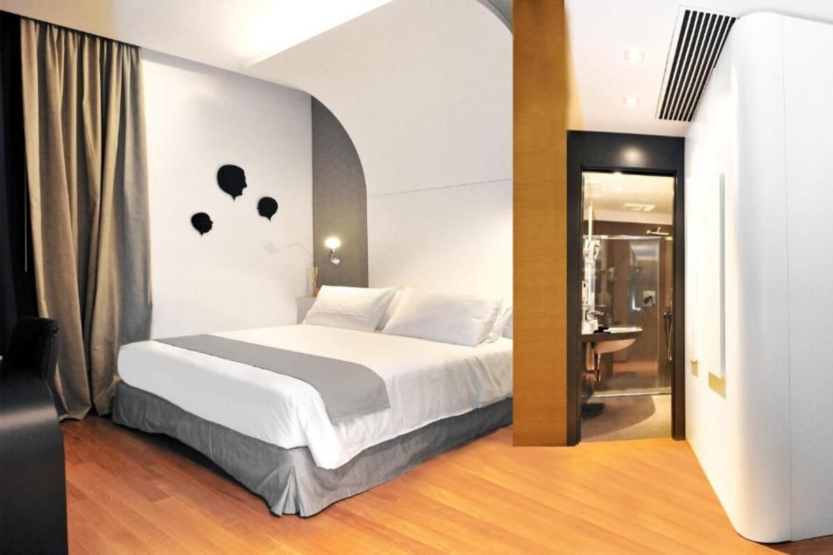 A modern hotel room with a large bed, a curved wall design, and a visible bathroom.