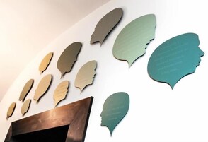 Una pared con recortes de distintas formas, algunos con texto, y un panel de madera debajo.