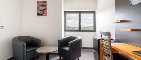 Una habitación moderna con dos sillones, una mesita redonda, un escritorio de madera y un televisor montado en la pared.
