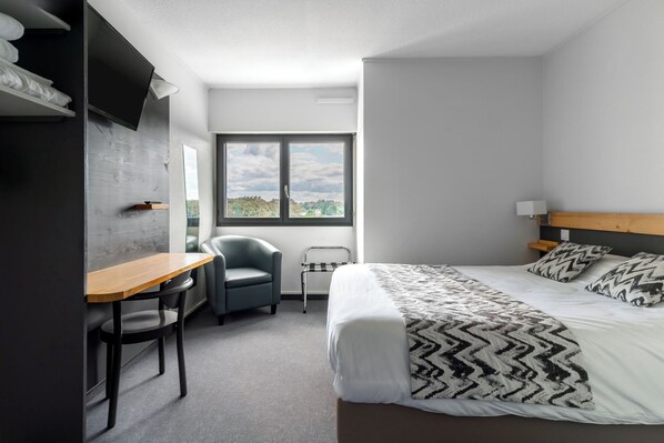 A modern hotel room with a bed, a desk, a chair, and a window with a view of greenery. - Abor Hôtel (Saint-Pierre-du-Mont)