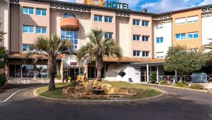 A hotel with a sign reading "ABOR HOTEL" and a landscaped front yard with palm trees and a rock feature. - Abor Hôtel (Saint-Pierre-du-Mont)