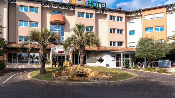 A hotel with a sign reading "ABOR HOTEL" and a landscaped front yard with palm trees and a rock feature.