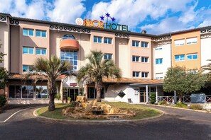 A hotel with a sign reading "ABOR HOTEL" and a landscaped front yard with palm trees and a rock feature.
