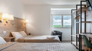 A hotel room with two beds, a desk, a chair, a TV, and a window with a view of greenery.