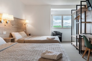 Habitación de hotel con dos camas, un escritorio, una silla, un televisor y una ventana con vistas a zonas verdes.