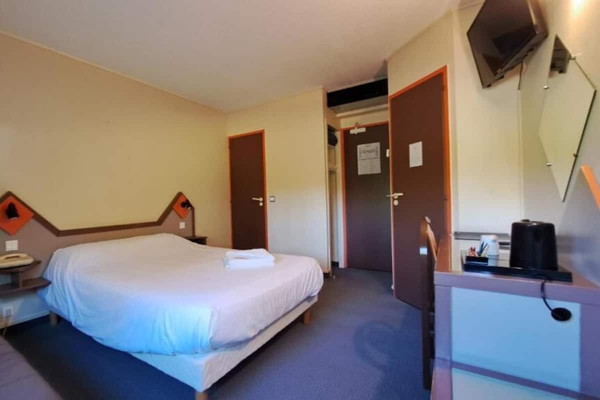 A hotel room with a single bed, a desk with a computer, a telephone, and a television.
